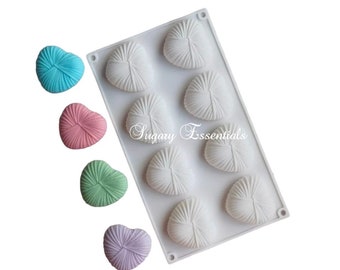May include: A white silicone mold with eight heart-shaped cavities, each with a textured design. Four colorful heart-shaped candies in blue, pink, green, and purple are displayed next to the mold. The text "Sugary Essentials" is printed on the mold.
