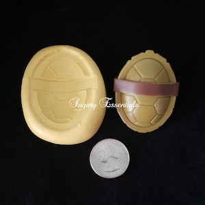 May include: Two silicone molds for making turtle shell shapes. The mold on the left is a flat, detailed shell. The mold on the right is a 3D shell with a brown band around the middle.