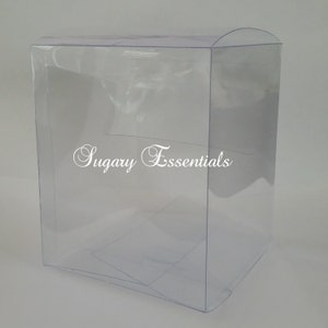 May include: A clear, transparent, rectangular plastic display box with a rounded top edge. The front panel features the white text Sugary Essentials printed in a cursive script font. The box is constructed from thin, flexible, see-through material.