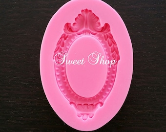 May include: Pink silicone mold shaped like an oval frame with ornate details. The mold is designed to create a cake or cookie decoration.