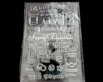 May include: Clear stamp set with get well soon themed images, including a soup can, bandaid, tissue box, and the text "Get well soon", "Bless you", "You're soup-er", "Stuck together", "Ouch! It's not fun being sick", "Have a soup-erb day!" and "Sneeze the day".