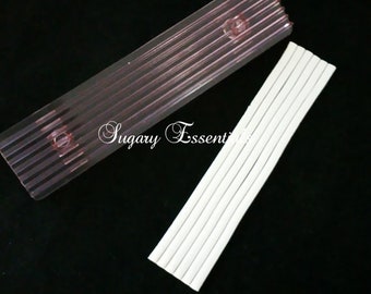 May include: A rectangular, clear, ribbed plastic tool with two circular indentations alongside a matching rectangular, white, ribbed plastic tool. The text Sugary Essentials is printed in white script across the center of the image.