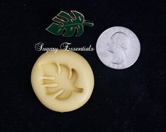 May include: A silicone mold for making a monstera leaf design. The mold is yellow and has a monstera leaf shape. A quarter is shown for size comparison.