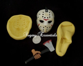 May include: A set of four silicone molds for making cake decorations. The molds are yellow and feature a hockey mask, a hand holding an axe, and two other shapes. The text "Sugary Essentials" is visible in the image.