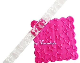 May include: A clear acrylic rolling pin with a star pattern embossed on the surface. The rolling pin is shown on top of a pink silicone baking mat with a star pattern.