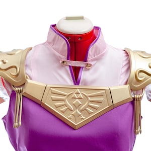 Puede incluir: Un disfraz de cosplay con un vestido morado y rosa, hombreras doradas y una placa pectoral. La armadura tiene dise&ntilde;os intrincados y borlas. El disfraz se exhibe en un maniqu&iacute;.
