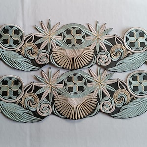 May include: Two embroidered appliques with a repeating pattern of stylized flowers, leaves, and circular designs. The appliques feature a color palette of black, light blue, beige, and white, creating a detailed and ornate design.