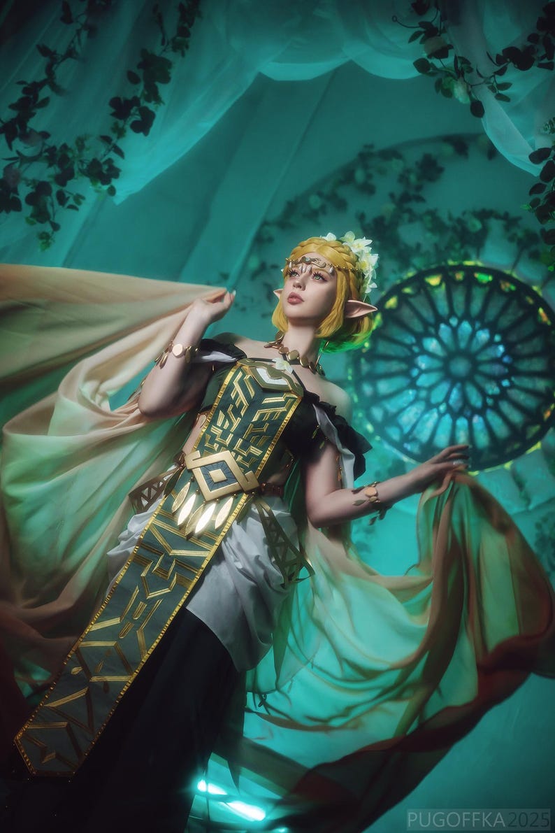 May include: A person in a cosplay costume with a gold headpiece, green and gold accents, and flowing fabric. The costume has a geometric design on the bodice. The background is a teal color with floral accents and a stained glass window.