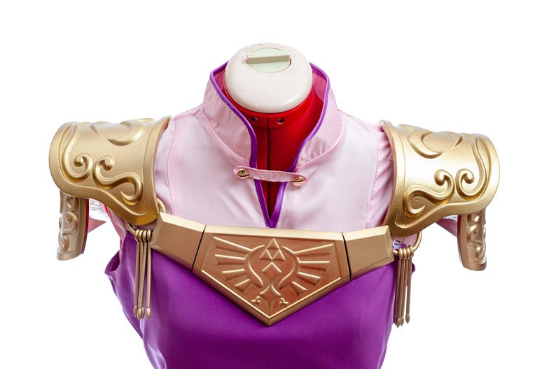 Puede incluir: Un disfraz de cosplay con una parte superior rosa y morada con detalles dorados. El disfraz incluye una armadura de hombro dorada adornada y una pieza de pecho dorada con un dise&ntilde;o geom&eacute;trico. El disfraz se exhibe en un maniqu&iacute;.