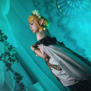 May include: A person in a fantasy-themed costume with a yellow wig, pointed ears, and a white and black dress. The background is a teal color with a stained-glass window design. The image has the text "PUGOFFKA 2023" in the bottom right corner.