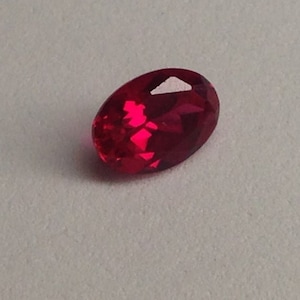 May include: A deep red oval-shaped gemstone with a faceted cut.