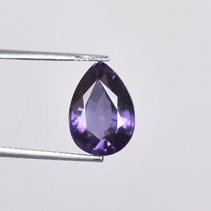May include: A pear-shaped amethyst gemstone with a deep purple hue. The gemstone is held in a pair of tweezers.