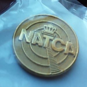 May include: A gold-colored pin with the acronym "NATCA" and a stylized image of an airport control tower.