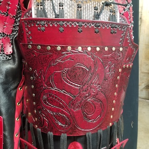 May include: Red leather armor with a dragon design and metal accents. The armor is worn over a chainmail shirt.