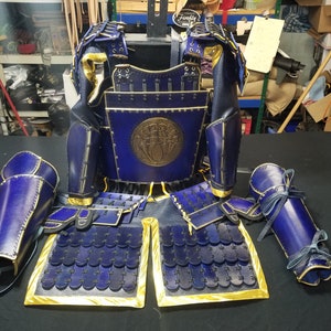 May include: A set of blue and gold samurai armor, including a chest plate, shoulder pads, and arm guards. The armor is decorated with a circular design on the chest plate.