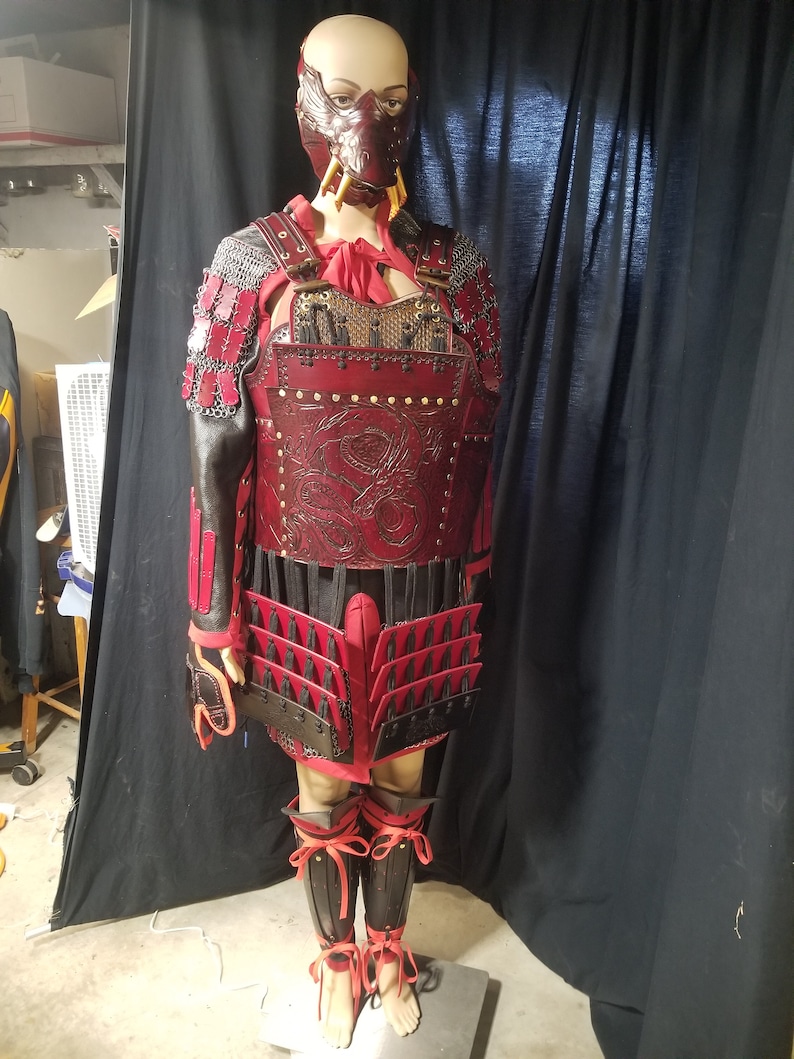 May include: A red and black leather samurai armor set with a dragon design. The armor includes a chest piece, skirt, and leg guards. The set is worn by a mannequin with a red and black mask.