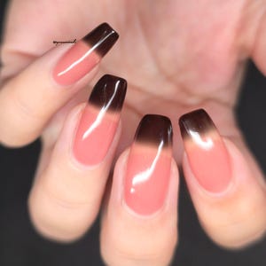 May include: Close-up of a hand with long, square-shaped nails. Each nail features a gradient design, transitioning from a light pink base to a dark brown tip. The nails are glossy and well-manicured, showcasing a modern nail art style.