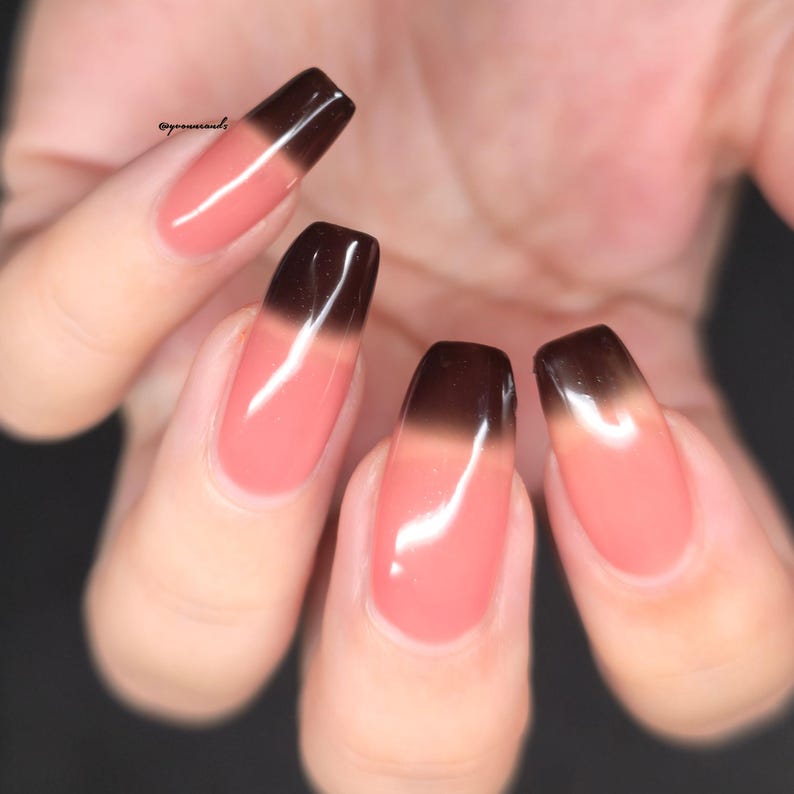 May include: Close-up of a hand with long, square-shaped nails. Each nail features a gradient design, transitioning from a light pink base to a dark brown tip. The nails are glossy and well-manicured, showcasing a modern nail art style.