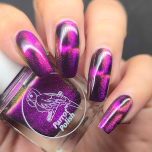 May include: Close-up of a hand with long, polished nails in a vibrant purple hue with a cat-eye effect. The nail polish bottle, labeled "Parrot Polish," is visible, featuring a parrot logo. The nails have a glossy finish.