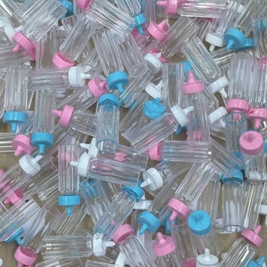 May include: A large pile of clear plastic baby bottles with pink and blue caps. The bottles are all the same size and shape, and they are arranged in a random pattern.