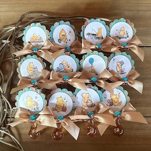 May include: Twelve Winnie the Pooh themed baby shower favors. Each favor is a round wooden cutout with a different Winnie the Pooh image. The cutouts are attached to a clear plastic pacifier with a gold ribbon.