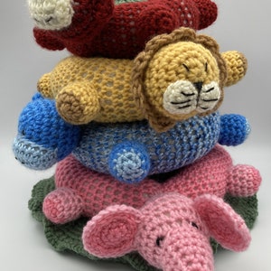 May include: A stack of crocheted animal rings, starting with a red monkey, followed by a yellow lion, a blue hippopotamus, and a pink elephant. The rings are all crocheted in a simple stitch and have a green leaf base.