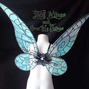 May include: A pair of teal blue fairy wings with black and white swirl designs. The wings are attached to a white mannequin torso. The text "Fairy Wings and Sparkly Things" is visible in the top center of the image.