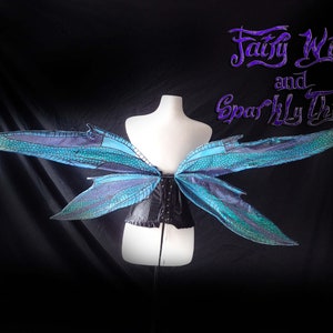 May include: A pair of blue and green fairy wings with a black corset. The wings are made of iridescent fabric and have a delicate, intricate design. The text "Fairy Wings and Sparkly Things" is written in purple at the top of the image.