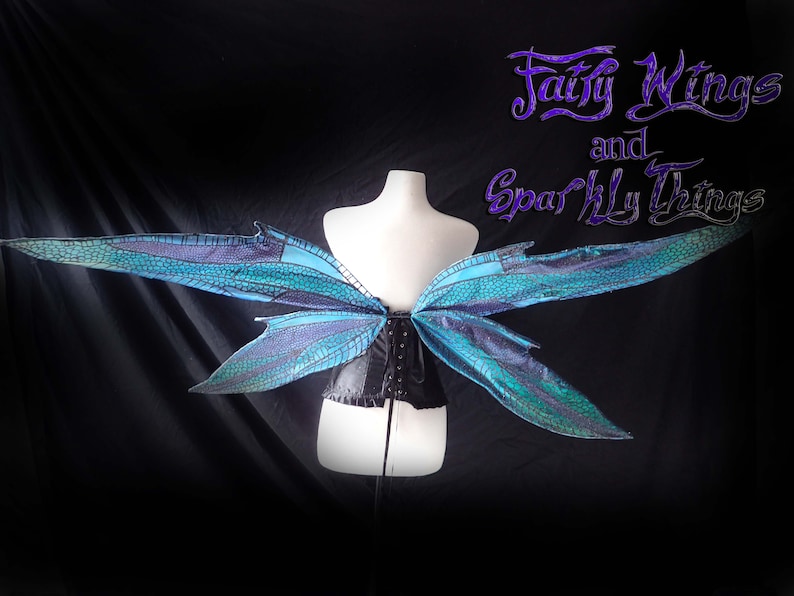May include: A pair of blue and green fairy wings with a black corset. The wings are made of iridescent fabric and have a delicate, intricate design. The text "Fairy Wings and Sparkly Things" is written in purple at the top of the image.