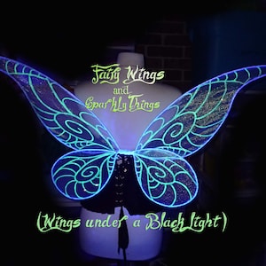 May include: Fairy wings with a black light effect. The wings are a vibrant blue with intricate swirling patterns and glitter accents. The text "Fairy Wings and Sparkly Things" and "(Wings under a Black Light)" are visible.