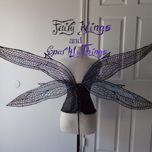 May include: A pair of large, iridescent fairy wings with a black lace design. The wings are attached to a black corset.