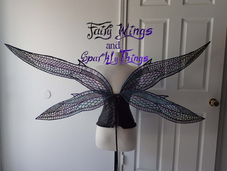 May include: A pair of large, iridescent fairy wings with a black lace design. The wings are attached to a black corset.
