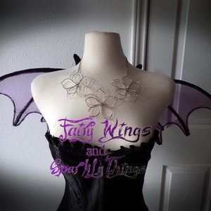 May include: A silver wire flower necklace with three flowers, worn on a mannequin with purple fairy wings. The text "Fairy Wings and Sparkly Things" is visible on the mannequin's bodice.