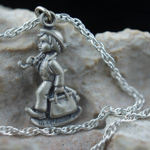 May include: A silver necklace featuring a charm of a boy carrying a suitcase. The charm is detailed and has a realistic look.