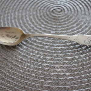 May include: A silver teaspoon with a rounded bowl and a long, slender handle. The handle is engraved with the initials "B.S."