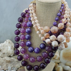 May include: A multi-strand necklace with large, round, faceted beads in shades of purple, pink, and peach. The beads are made of glass and have a sparkly finish.