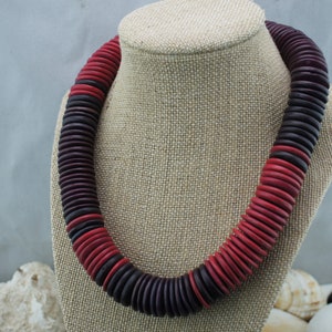 May include: A necklace made of wooden beads, with alternating red and dark purple colors. The beads are round and flat, and they are strung together in a simple pattern.