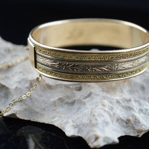 May include: A gold bangle bracelet with a delicate floral design and a matching chain. The bracelet is made of two-toned gold, with a yellow gold band and a white gold floral design.
