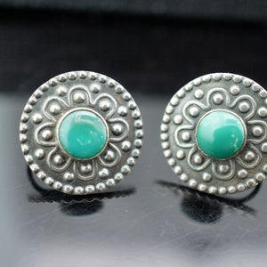 May include: A pair of silver earrings with turquoise stones set in a circular design.