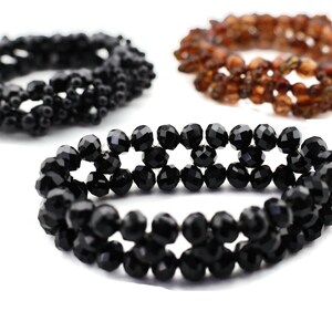 Könnte beinhalten: Drei Perlenarmbänder, eines schwarz, eines braun und eines klar. Die Armbänder bestehen aus kleinen, facettierten Perlen.