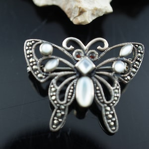 Op de afbeelding: Een zilveren vlinder broche met marcasiet en parelmoer accenten. De vlinder heeft een gedetailleerd ontwerp en is een prachtig sieraad.