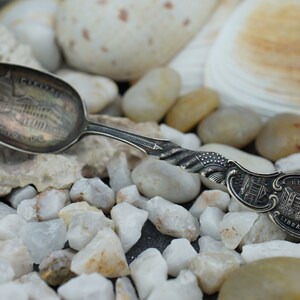 May include: A silver souvenir spoon with a detailed image of a building and the text "The Capitol" on the front. The back of the spoon has an image of a building with the text "New Library".