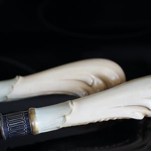 May include: Two ornate silver serving utensils with ivory handles. The handles are carved with a swirling design and have a gold trim.