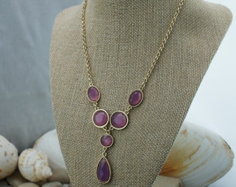 May include: A gold chain necklace with a pendant featuring a teardrop-shaped purple stone. The necklace has five round purple stones.