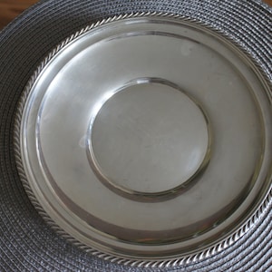 May include: A silver serving tray with a rope-like border. The tray is round and has a raised centre.