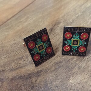 Può includere: Due spille dorate con smalto nero, rosso, verde e giallo. Le spille presentano un simbolo di carta da gioco di picche e il testo "ALL-AMERICAN REGIONAL CLEVELAND 1970".
