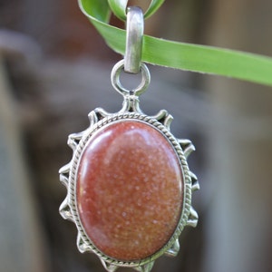 May include: A silver pendant with a reddish-brown oval stone set in a decorative silver frame.