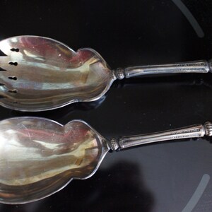 May include: A silver salad serving set with a fork and spoon. The handles are made of a white material with a decorative pattern.
