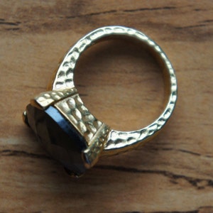 May include: A gold ring featuring a large, dark, faceted gemstone. The ring band has a textured, hammered finish.
