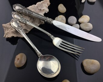 May include: A set of three silver-plated utensils, including a fork, a spoon, and a knife. The utensils have ornate handles with floral designs.